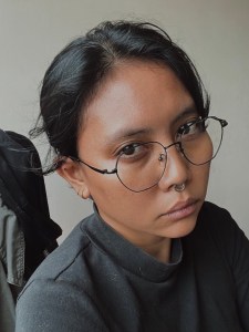 A stern-looking individual wearing glasses and black clothes.